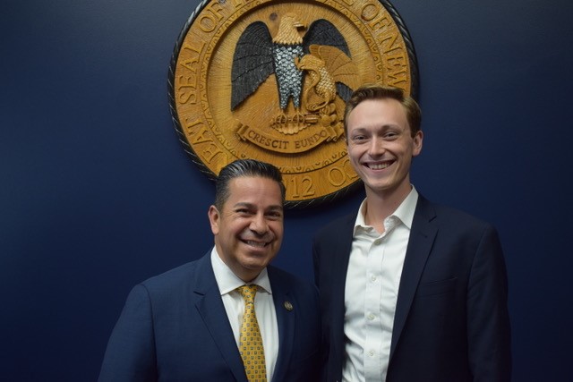 Assistant Speaker of the House Ben Ray Luján with Tomas Wesley Green in front of the seal of New Mexico