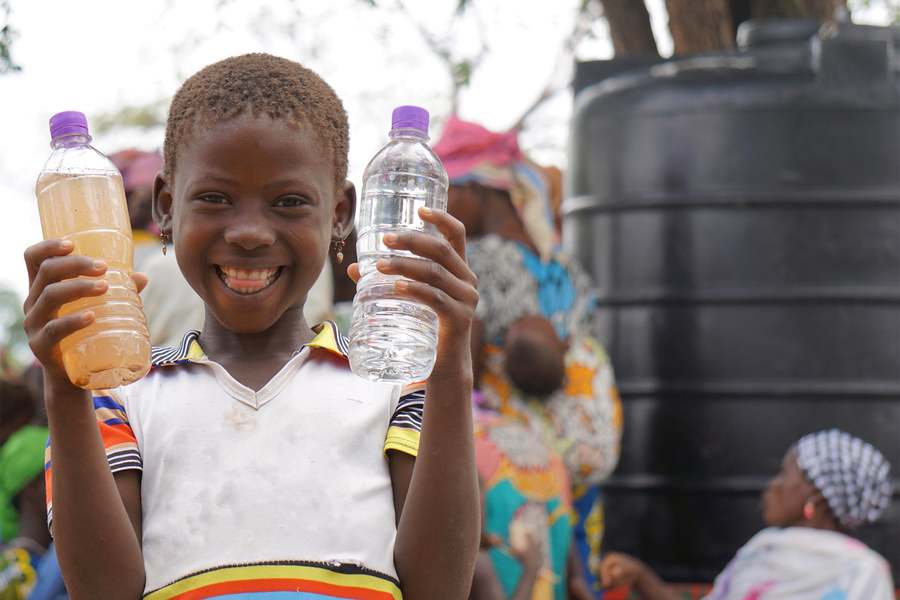 A child in Ghana holds bottles of unclean and purified water. The origin of the image is Saha Global.